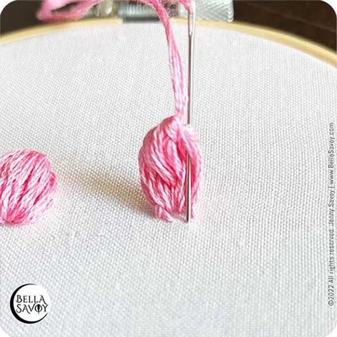 needle pushing down through popcorn lazy daisy stitch and into fabric
